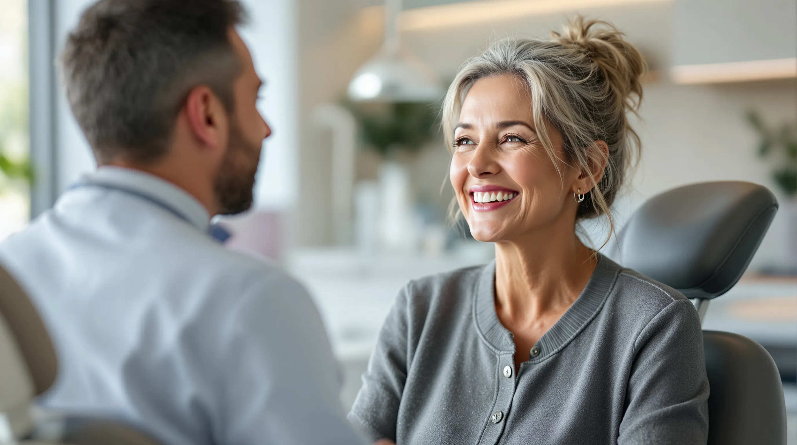 A woman speaking confidently and smiling in a bright dental office while a dentist listens, illustrating clear speech after dental implants